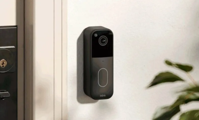 Blink video doorbell mounted on a white wall next to a modern door lock.