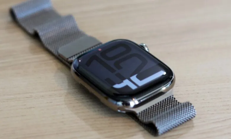 Close-up of a modern smartwatch with a metallic Milanese loop band on a wooden surface.