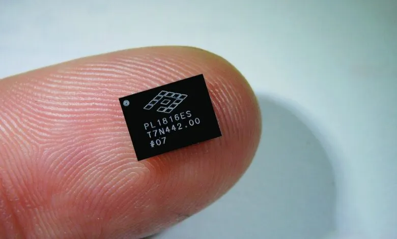 A tiny black microchip with white text and a logo rests on a human fingertip.