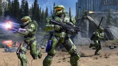 Master Chief and other Spartans in combat on a rocky, forested terrain.