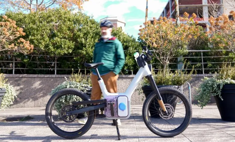 Modern white e-bike parked on sidewalk with blurred man in background.