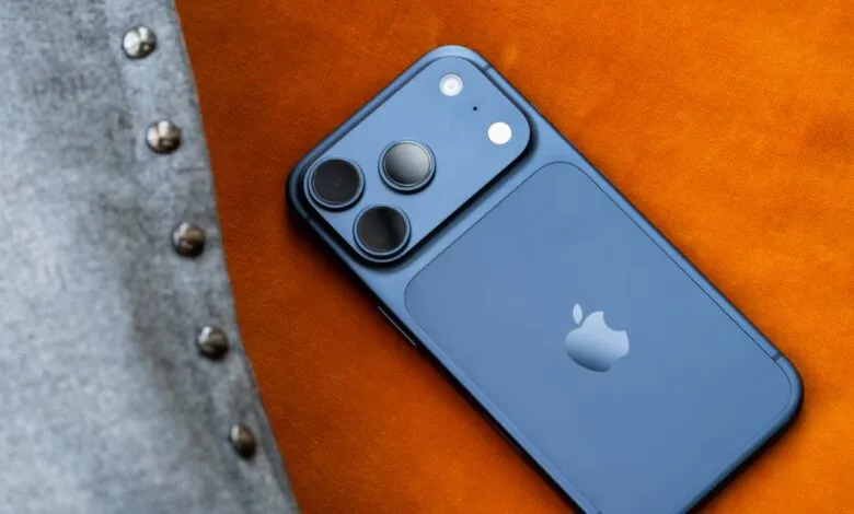 Blue iPhone with triple camera system on orange fabric next to gray jacket.