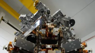 Complex spacecraft module with metallic panels and intricate wiring, viewed from below.