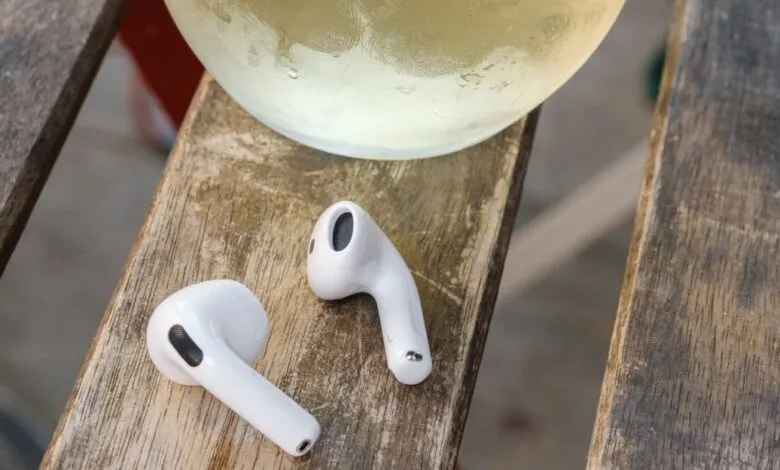 White wireless earbuds next to a glass of white wine on a wooden table.