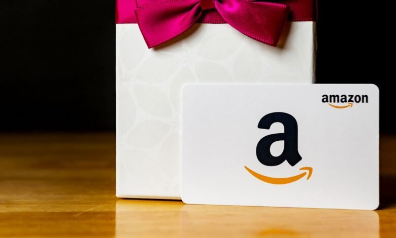 An Amazon gift card rests in front of a white gift box with a pink bow.