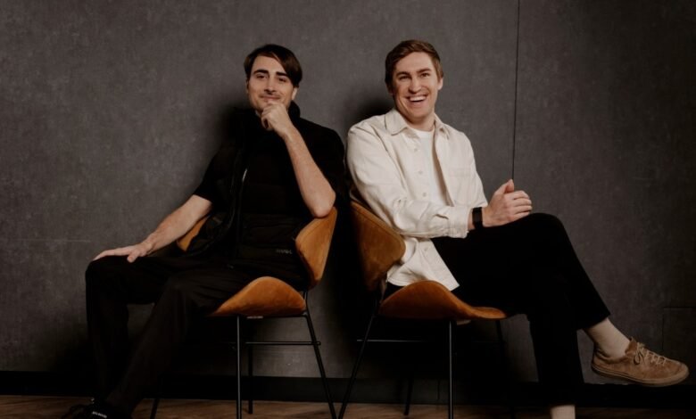 Two men, co-founders of ElevenLabs, sitting on chairs against a dark textured wall.