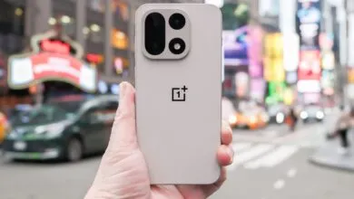 Close-up of a light gray OnePlus smartphone held in a hand, with a blurred Times Square background.
