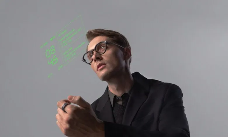 Man in glasses looking up at a green holographic display showing calendar and time.