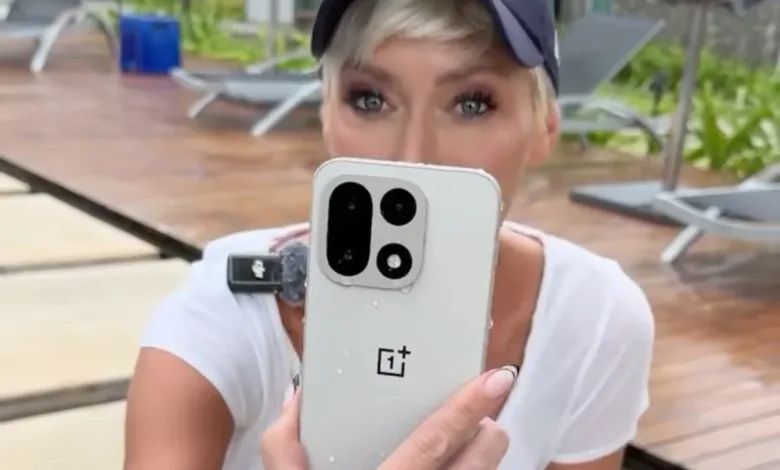 Woman holds up OnePlus phone in wet outdoor setting.