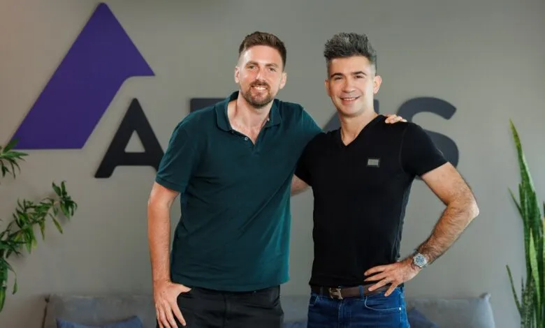 Two smiling men stand in front of the Armis logo, one with his arm around the other.