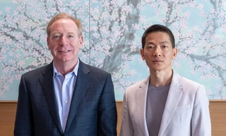 Brad Smith and Mohamed Alabbar pose for a photo in front of a cherry blossom mural.