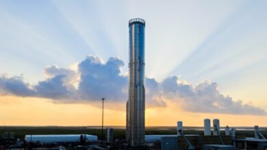 A tall, silver rocket stands against a sunset sky with dramatic sunbeams.