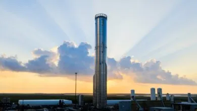 A tall, silver rocket stands against a sunset sky with dramatic sunbeams.