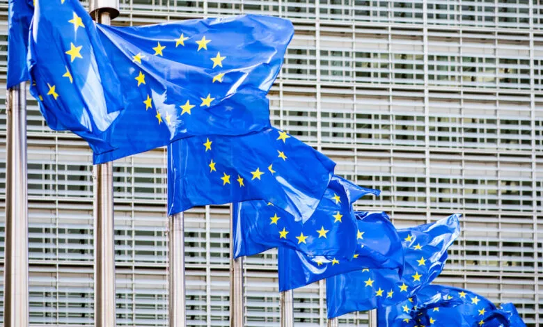 Multiple European Union flags waving in front of a modern building.