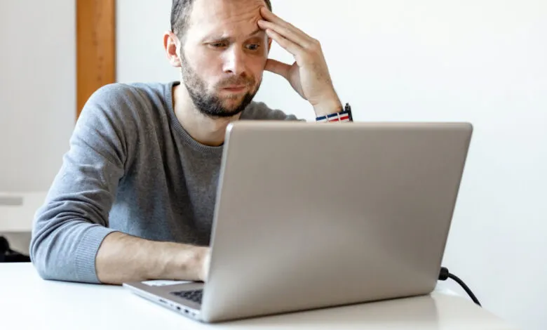 Man with beard looking stressed while working on a laptop