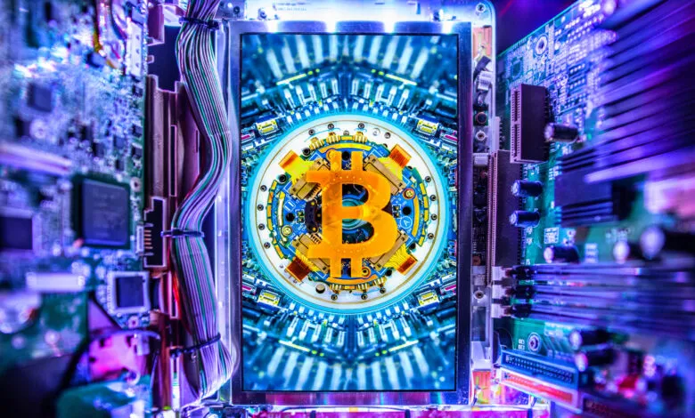 Close-up of a Bitcoin symbol on a computer motherboard with glowing blue and purple lights.