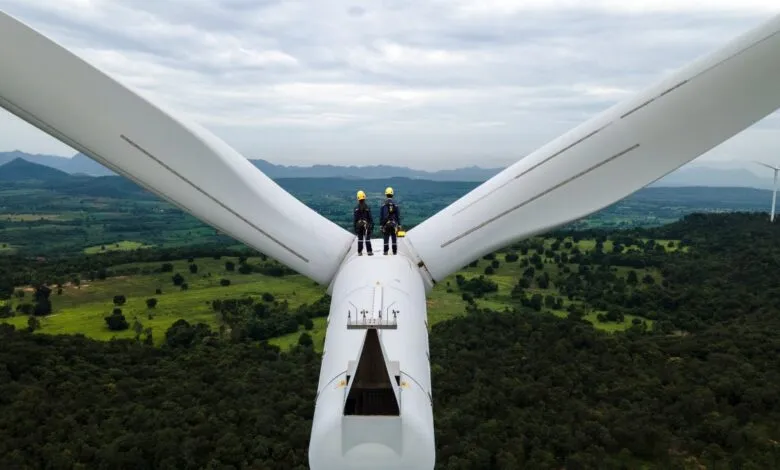 Two workers stand atop a wind turbine, inspecting the blades.