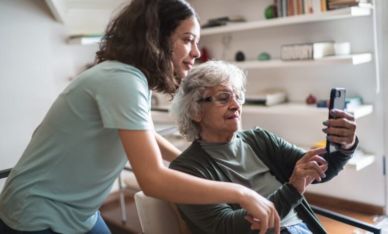 Young woman helps senior woman use smartphone indoors.