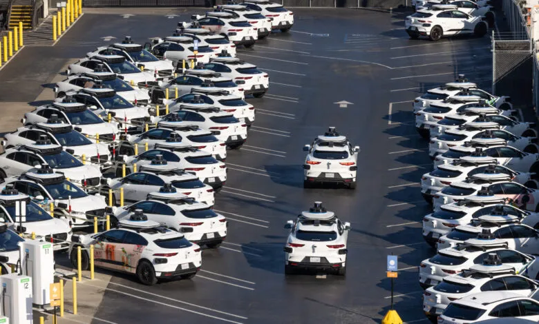 Rows of white Waymo self-driving Jaguar I-PACE vehicles parked in an outdoor lot.