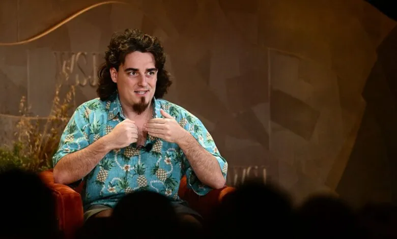 Man with curly hair and goatee wearing a pineapple shirt speaks on stage.
