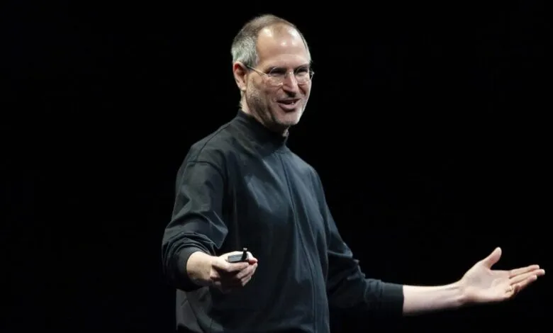 Steve Jobs presenting on stage, holding a clicker and gesturing with his hands.