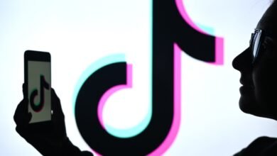 Silhouette of a person holding a smartphone with the TikTok logo, in front of a large TikTok logo.