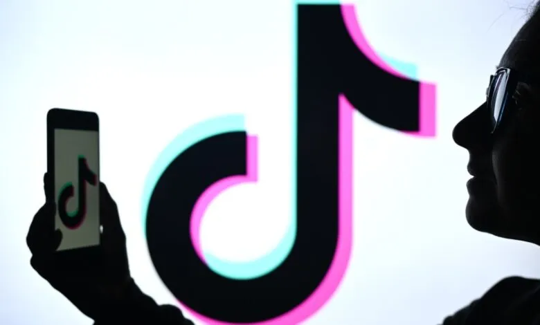 Silhouette of a person holding a smartphone with the TikTok logo, in front of a large TikTok logo.