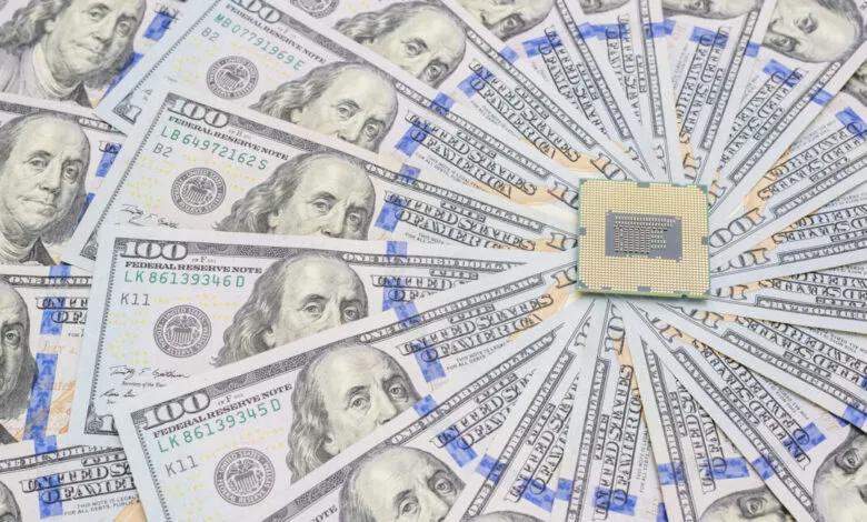A computer microchip rests on a fan of U.S. one hundred dollar bills.