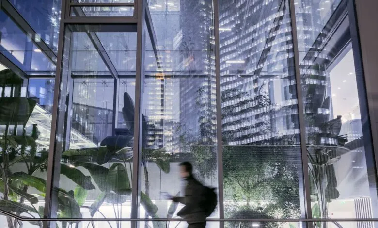 Blurry figure walking past large indoor plants with reflections of modern skyscrapers in glass.