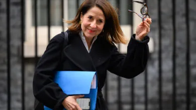 Liz Kendall smiles, holding glasses and a blue folder.