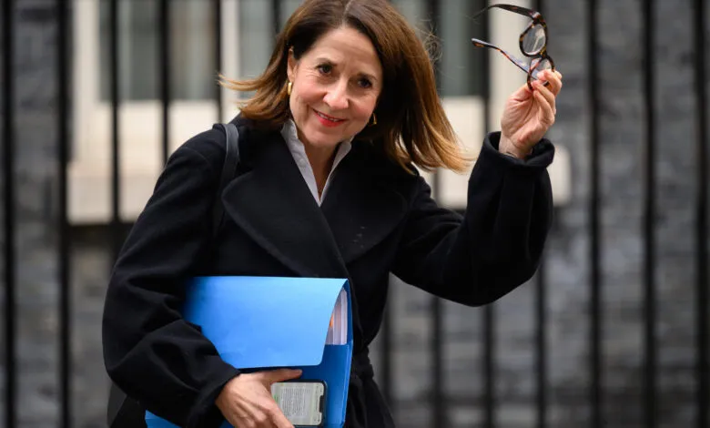 Liz Kendall smiles, holding glasses and a blue folder.