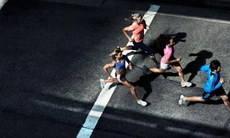 Four runners race down a street, casting long shadows in the sunlight.