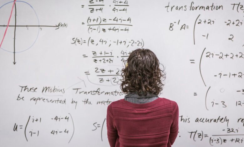 A person with curly hair looks at complex mathematical equations written on a whiteboard.