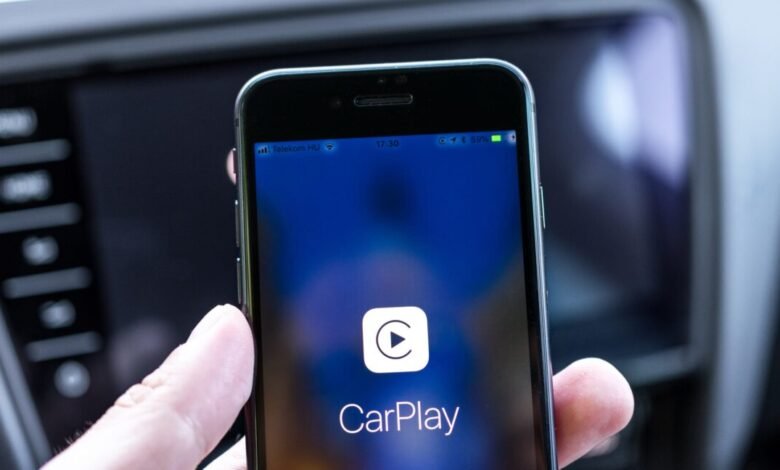 Close-up of a hand holding an iPhone displaying the Apple CarPlay interface.