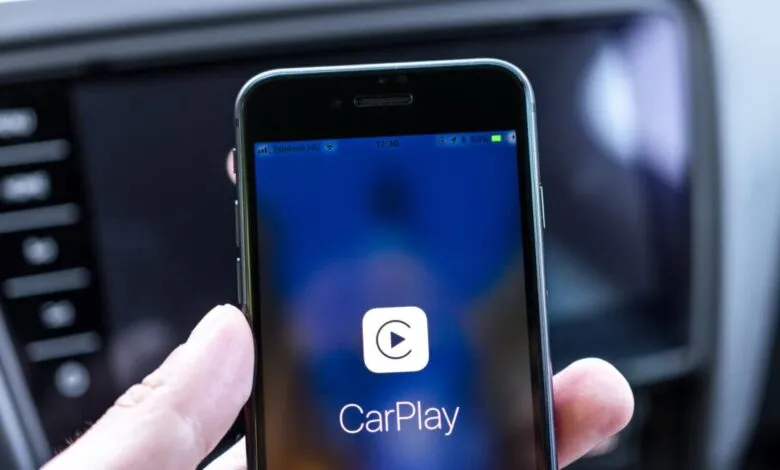 Close-up of a hand holding an iPhone displaying the Apple CarPlay interface.