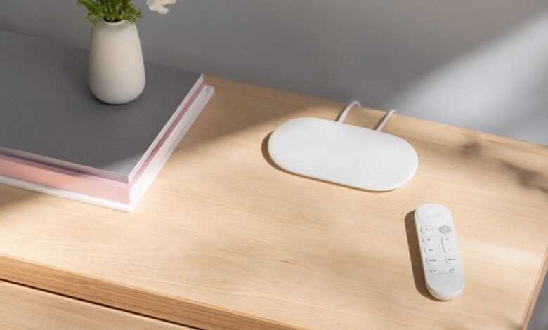 Google Chromecast with Google TV device and remote on a wooden surface.