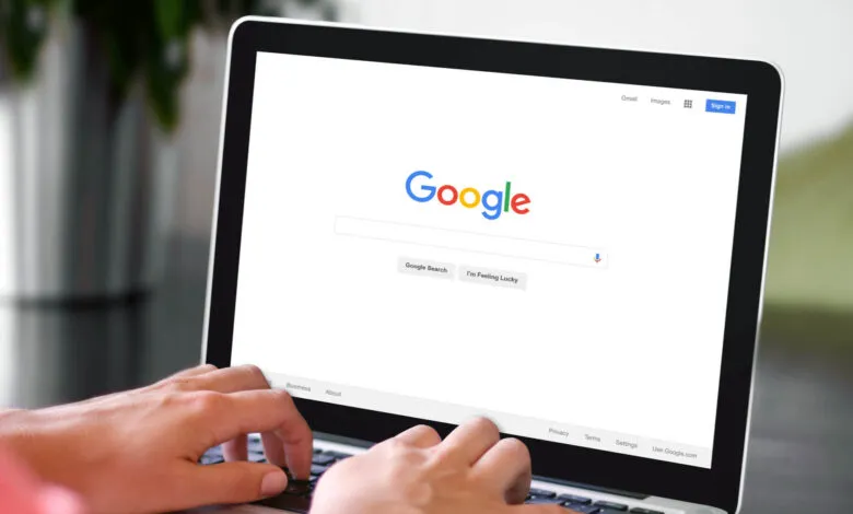 Person's hands typing on a laptop displaying the Google search engine homepage.