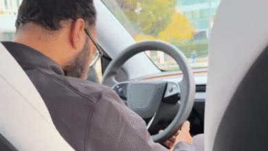 Man wearing glasses driving a car, holding the steering wheel.