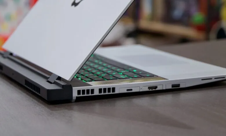 Close-up of a white gaming laptop with illuminated green keyboard and ports.