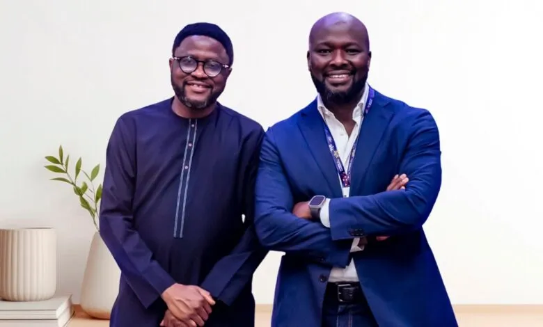 Two men in professional attire smiling at the camera, one in a blue suit, the other in traditional dark clothing.