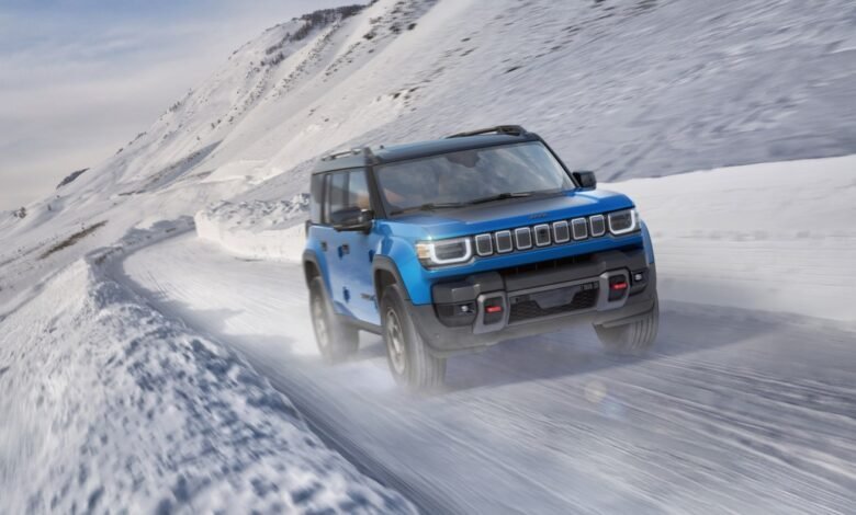 A blue Jeep SUV drives on a snow-covered mountain road.