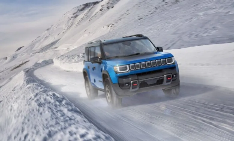 A blue Jeep SUV drives on a snow-covered mountain road.