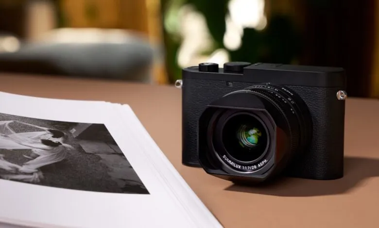 Black Leica Q3 Monochrom camera next to a stack of black and white photographs.