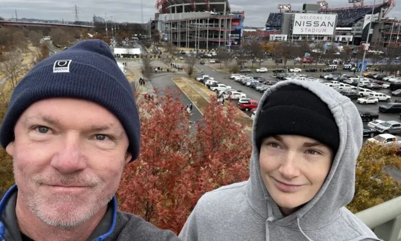 Two people pose in front of Nissan Stadium, Nashville, on an overcast day.