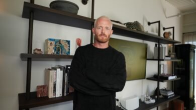 Man with blonde hair and beard stands with arms crossed in modern room.