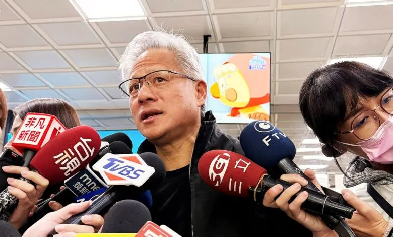 Man with glasses speaking to reporters surrounded by microphones.
