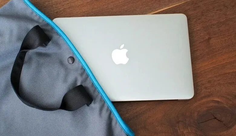 Silver Apple MacBook laptop partially in a grey tote bag with blue trim.