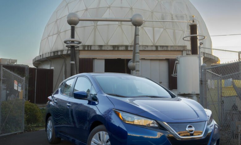 Blue Nissan Leaf parked in front of a large geodesic dome testing facility with electrical equipment.