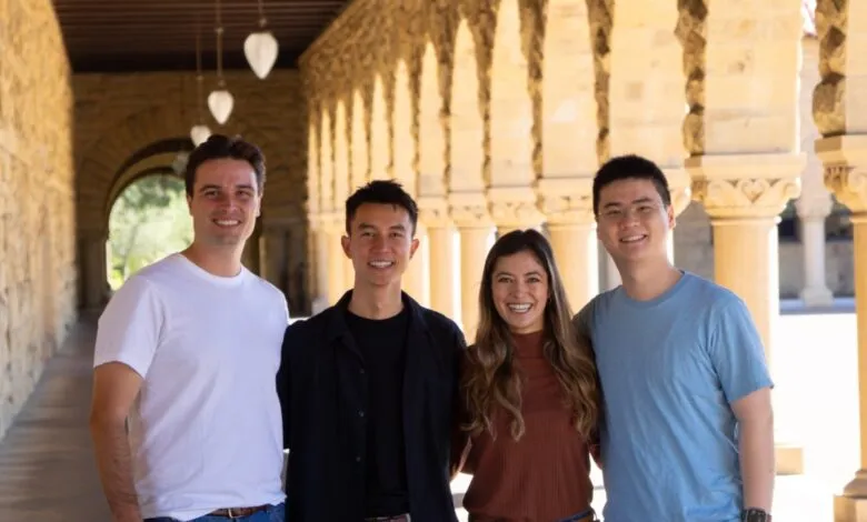 Four smiling young adults stand together in an arched walkway with stone columns.
