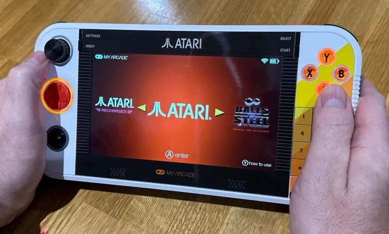 Atari handheld console displaying game selection screen, held by two hands.